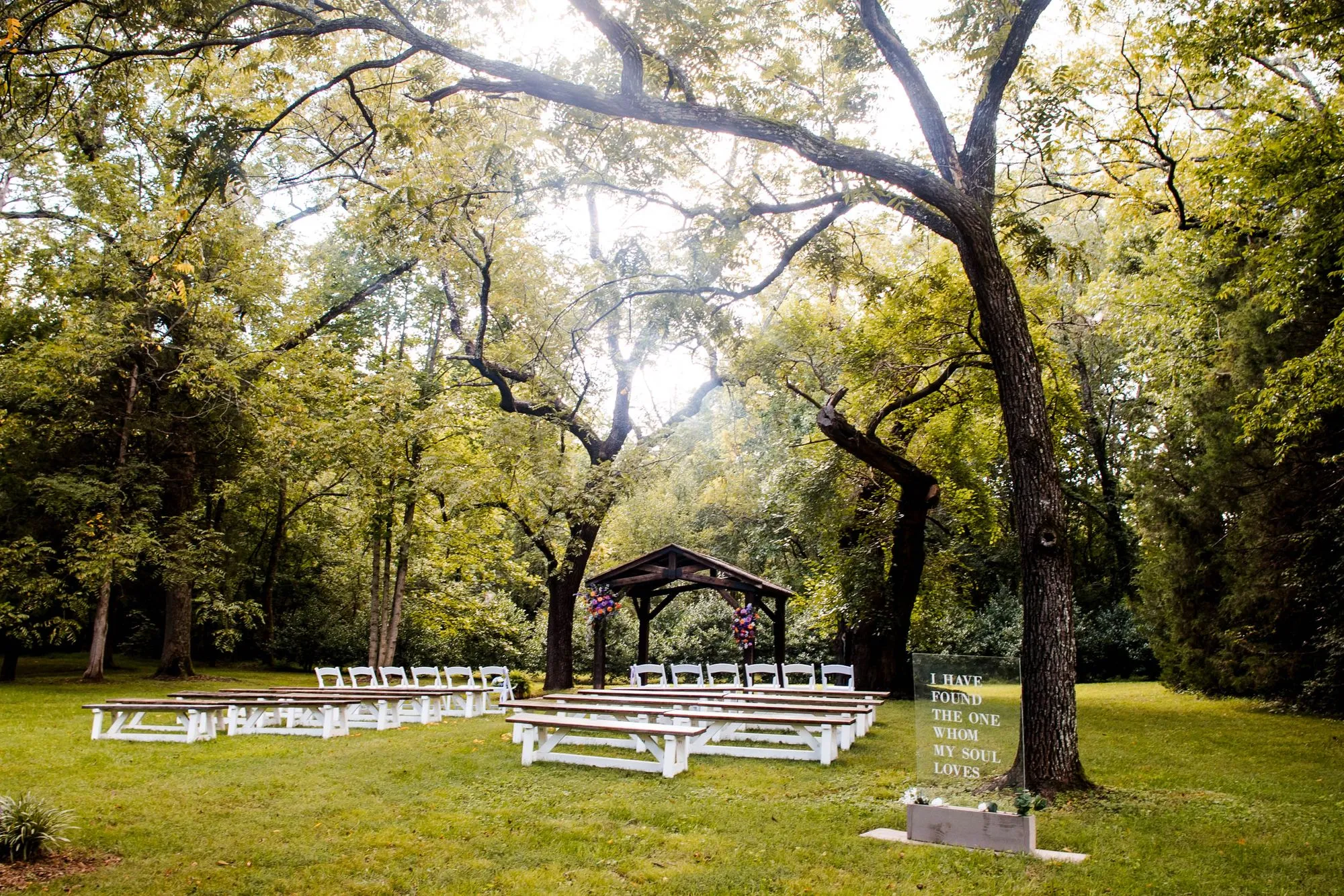 Ceremony benches beneath the historic walnut trees and wooden pavilion at The Heritage Barn