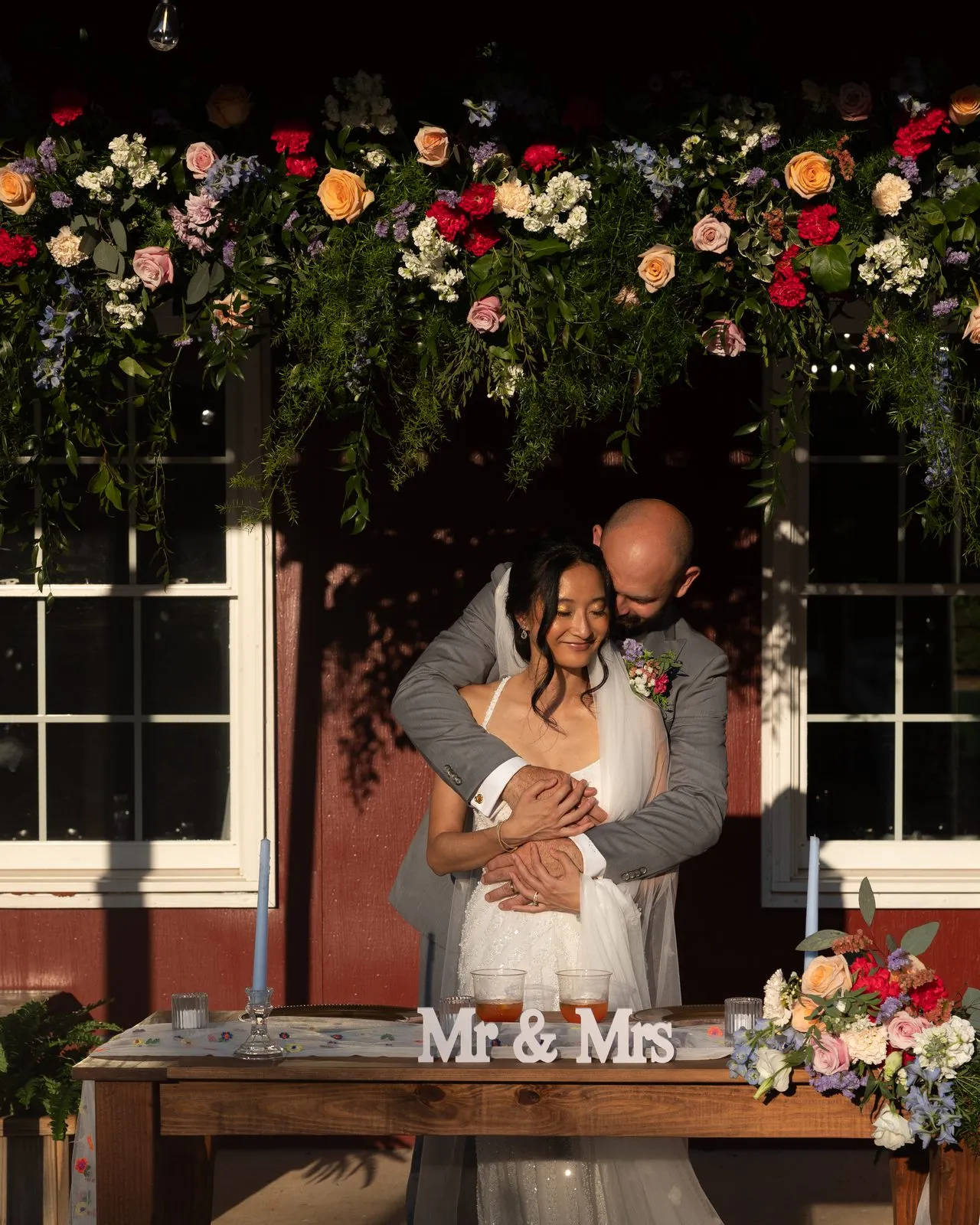 Couple at their sweetheart table beneath a lush floral garland at The Heritage Barn in Conover, NC
