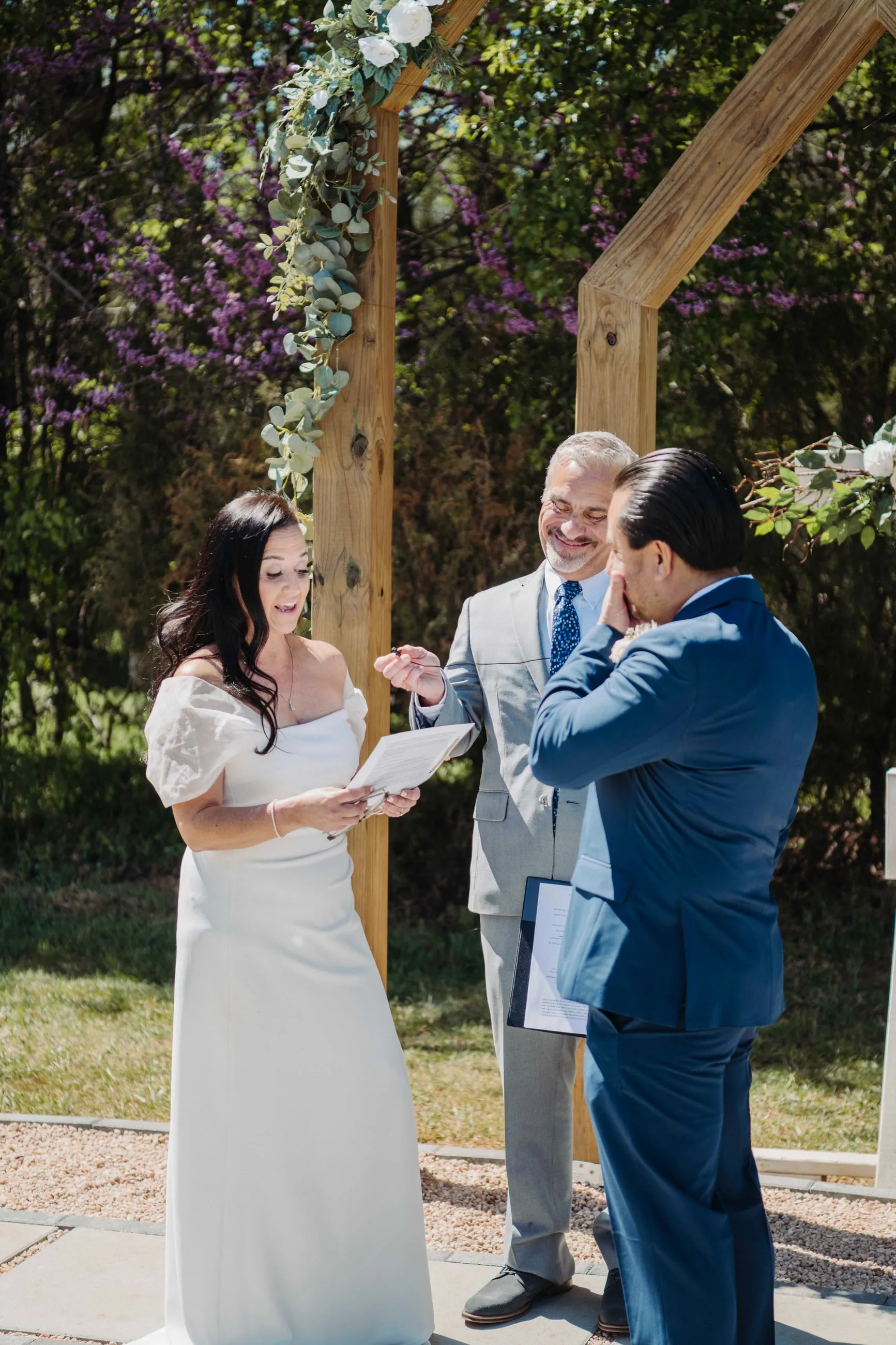 Couple exchanging vows during an outdoor ceremony beneath the wooden arbor at The Heritage Barn