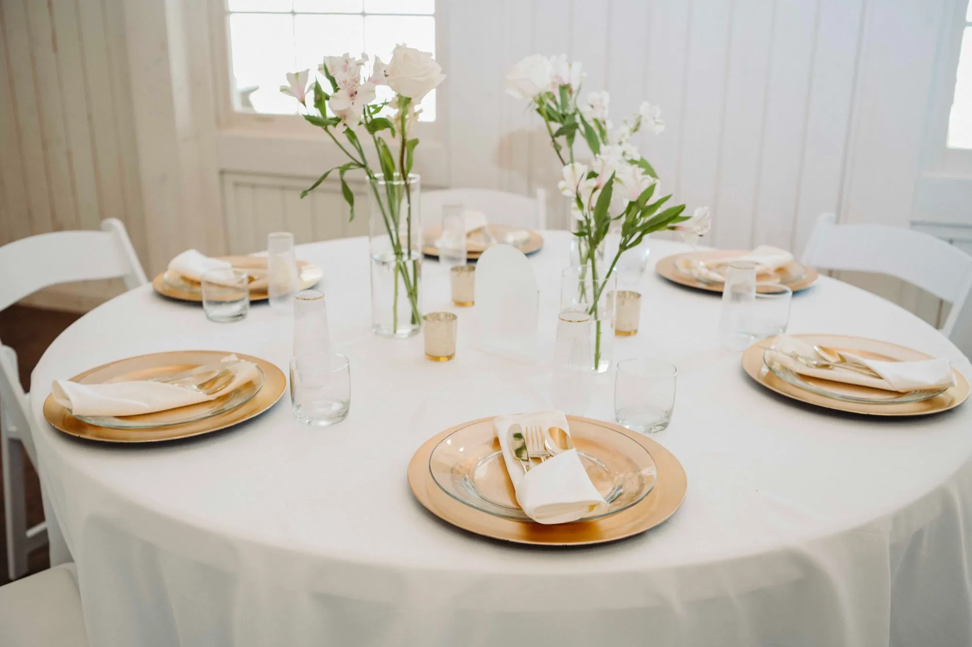 Reception table set with gold chargers and white florals inside The Heritage Barn