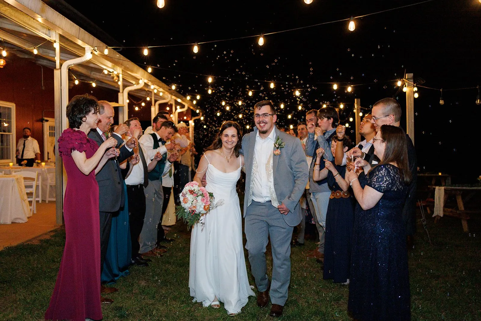 Couple walking out under string lights during a nighttime exit at The Heritage Barn