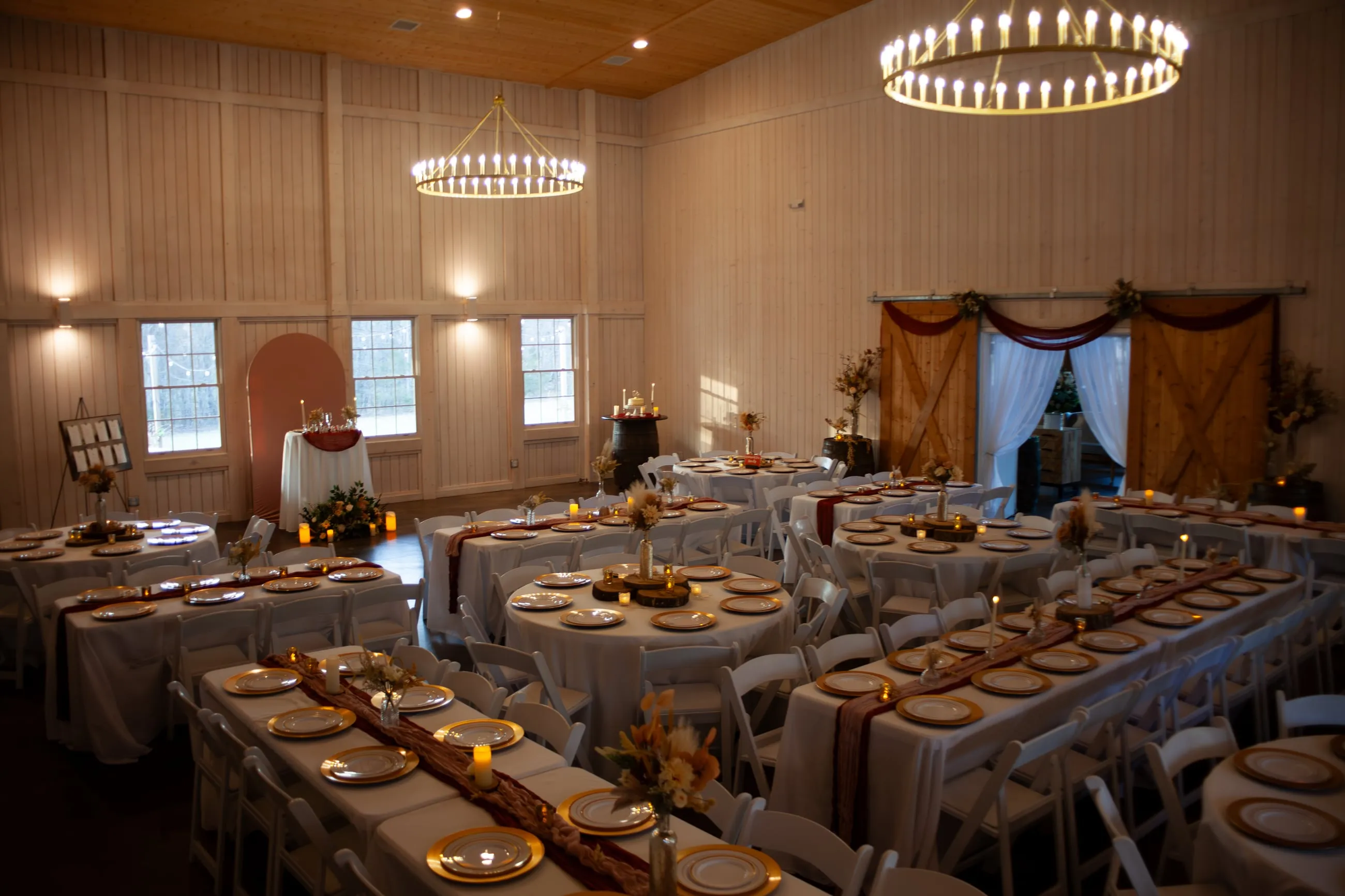 Updated barn reception space with round tables, greenery, and warm chandelier lighting at The Heritage Barn